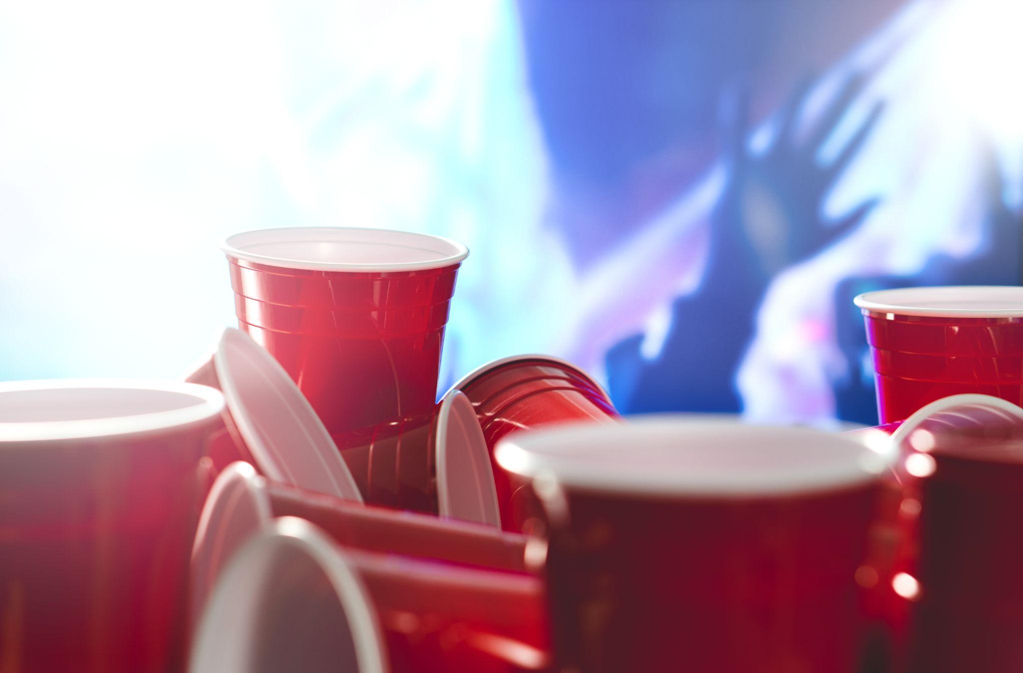 Many red party cups with blurred celebrating people in the background.