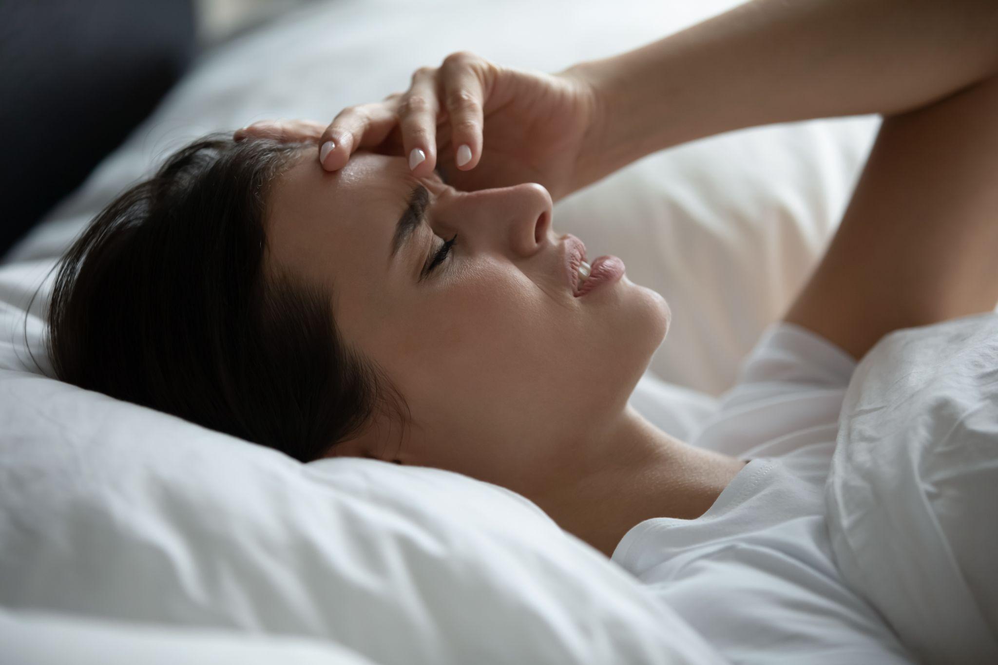 Sad female spending time in bed lying in pillows touching forehead