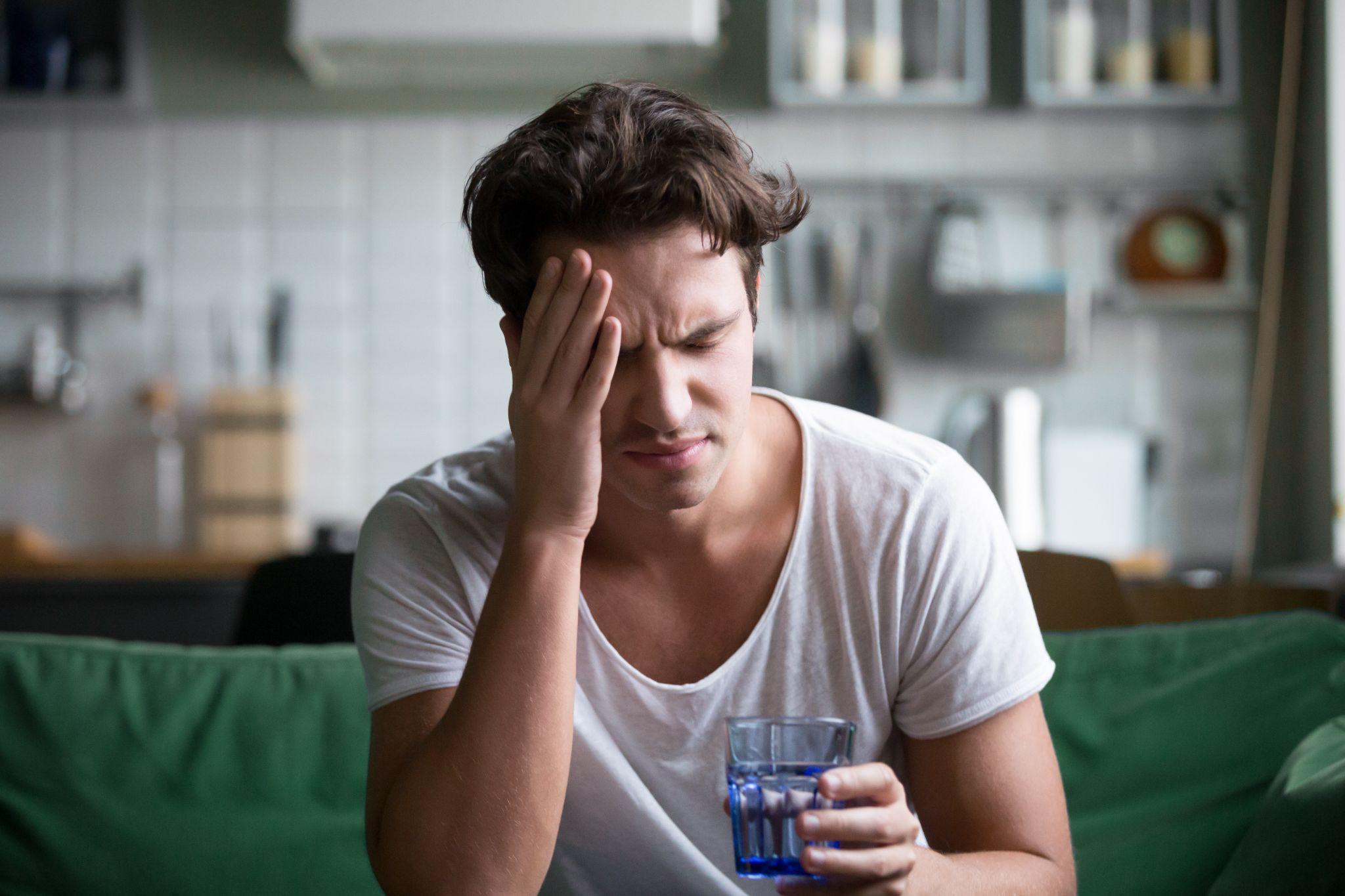 Young stressed person sitting on sofa with closed eyes touch head, having head ache