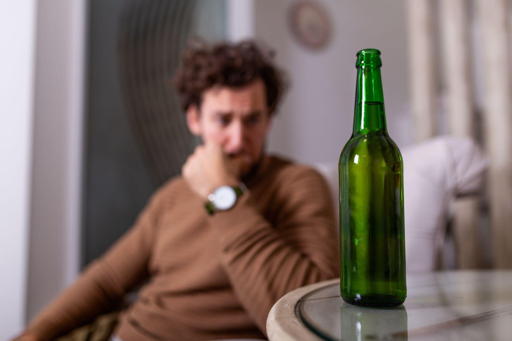 Alcoholic man reaching for bottle of beer, Man drinking home alone.