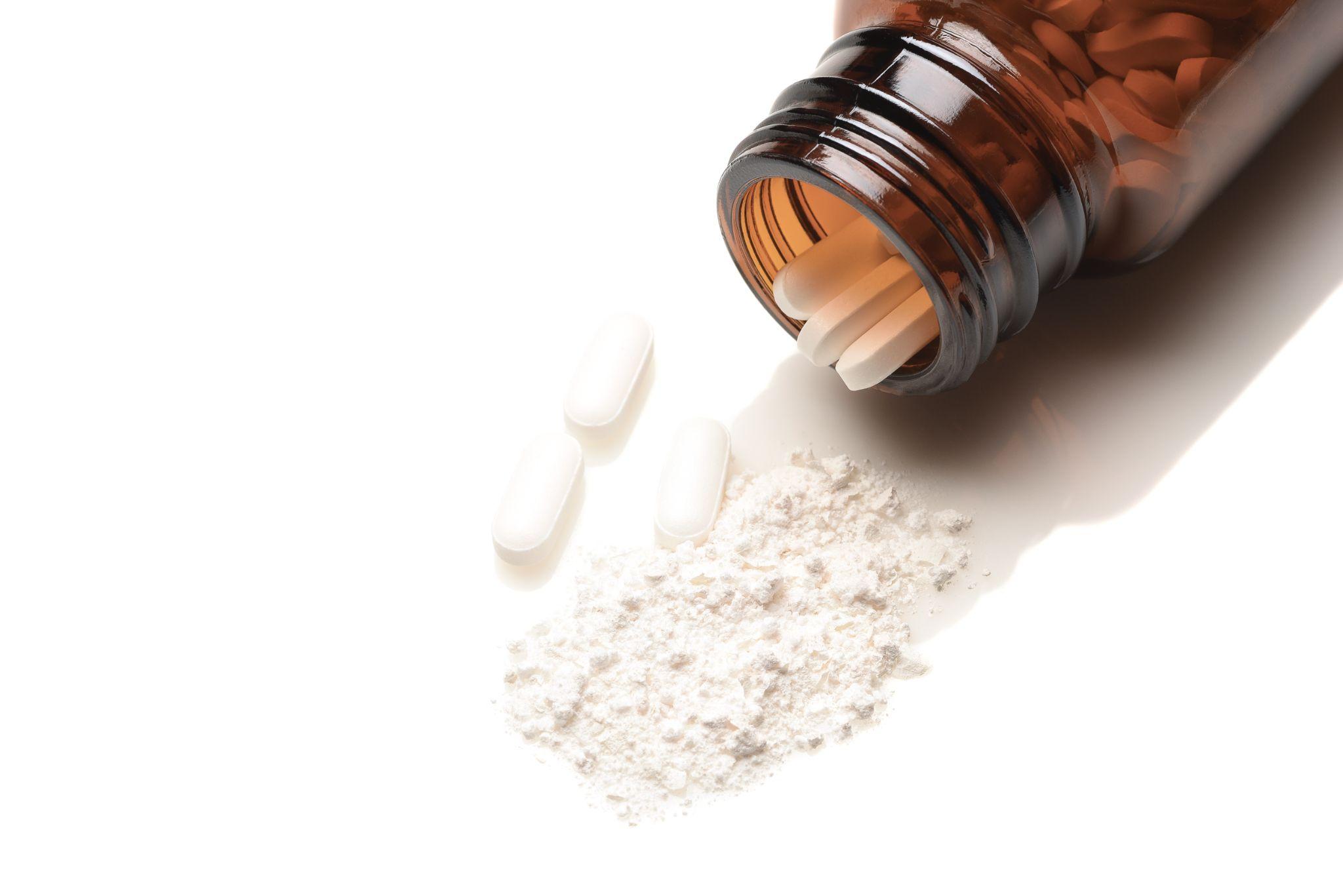 Opioid Crisis Concept: Closeup of an apothecary bottle on its side with a white powder from crushed pills spilling out.