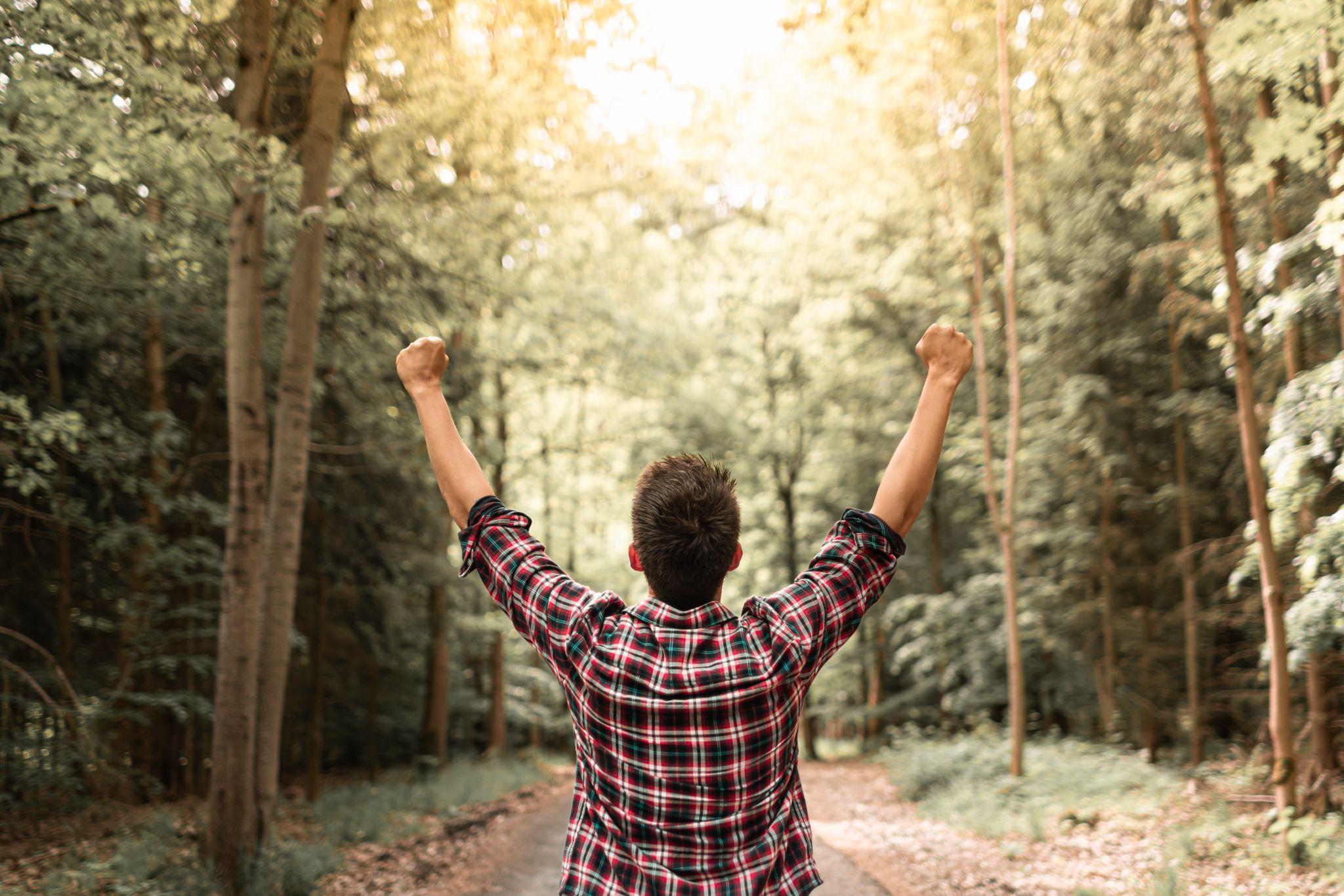 Happy strong young man with raised arm raised in autumn forest surrounded by beautiful nature
