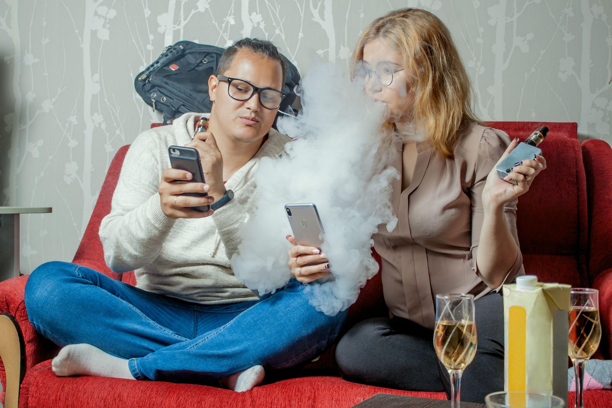 Students relaxing at home, showing to eachother their phones and vaping