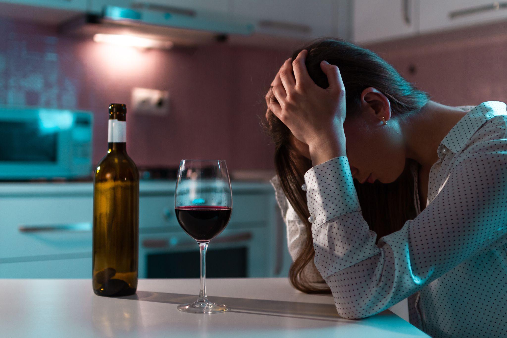 Unhappy, lonely, young woman with red wine is drinking alone at home in evening.