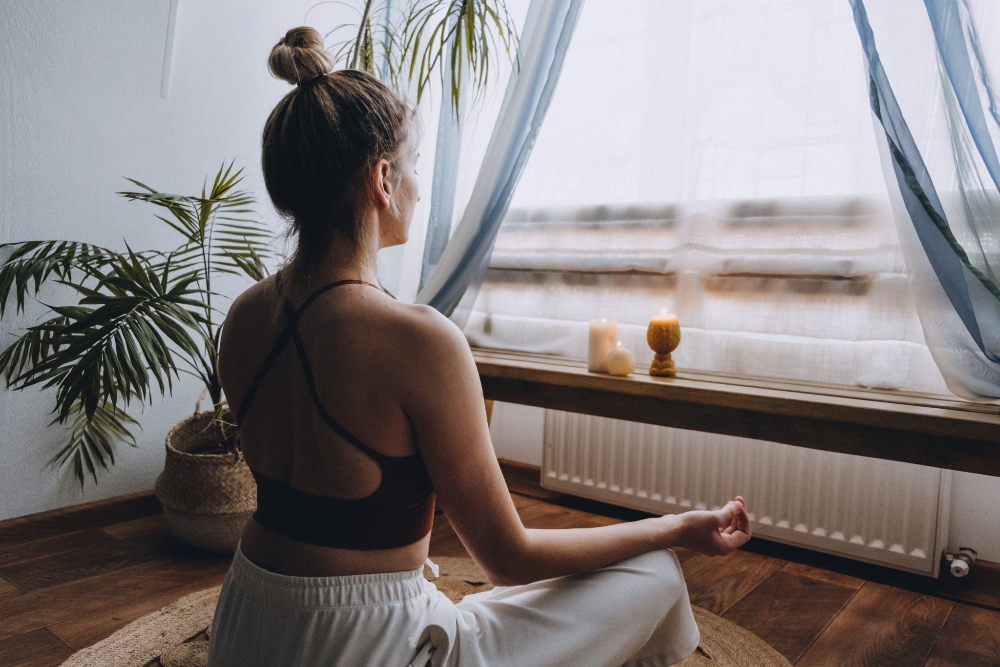 Young woman sitting on the floor, lights candles, enjoy meditation, do yoga exercise at home.