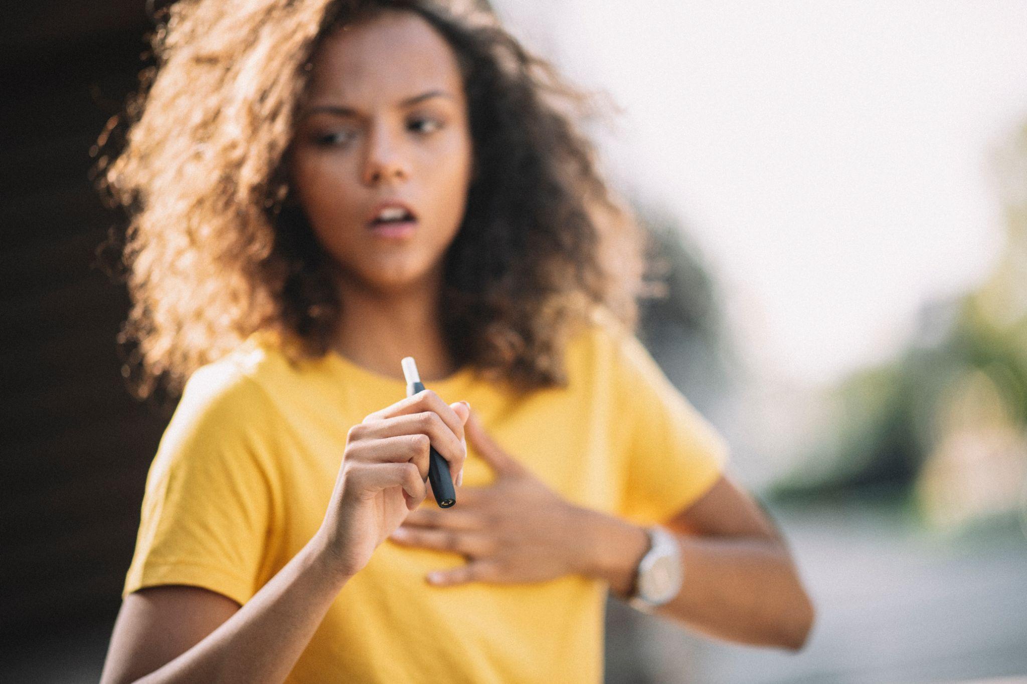 Afro girl smoking e-cigarette and coughing