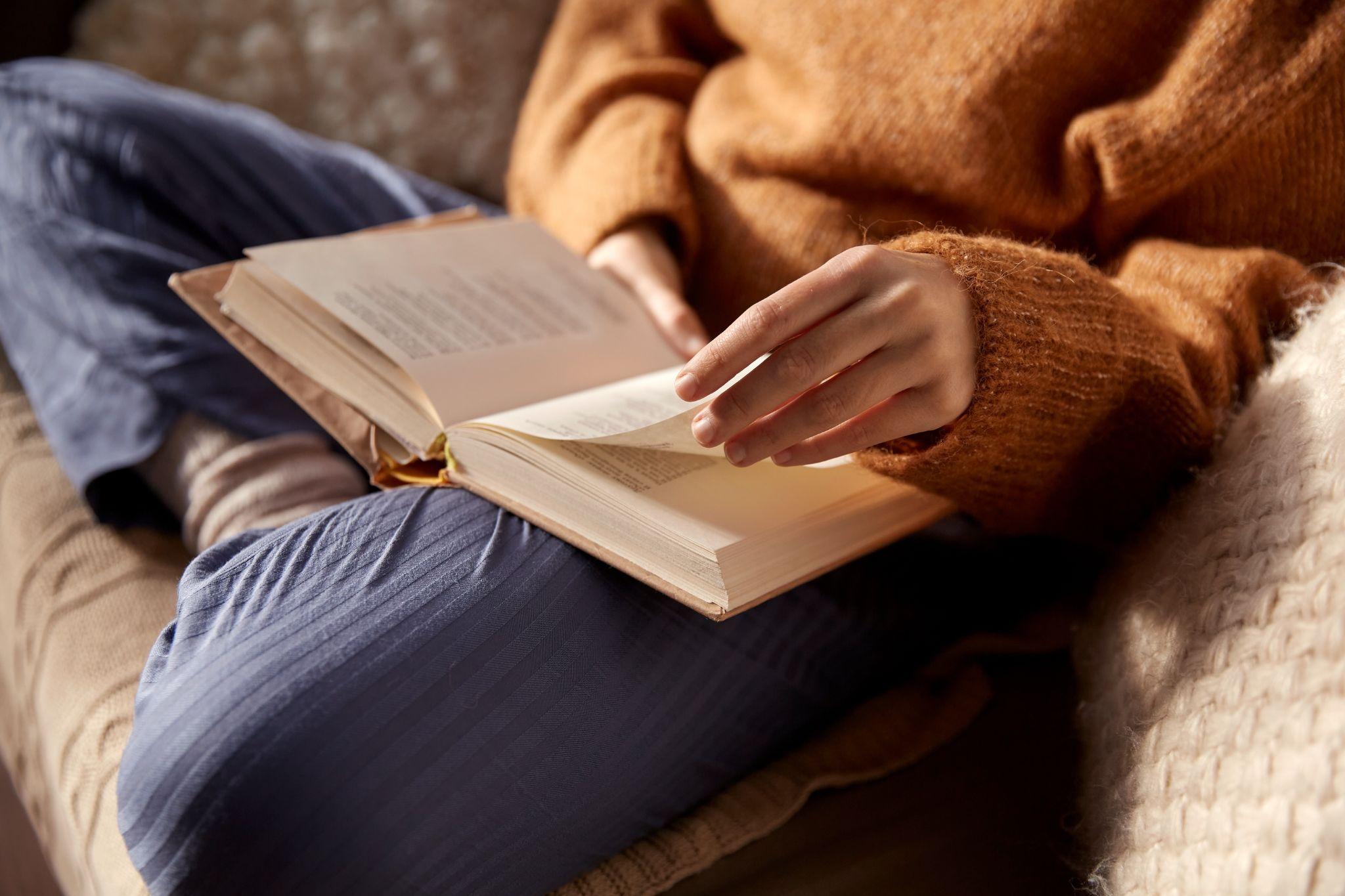 close up of woman in warm sweater reading book at home
