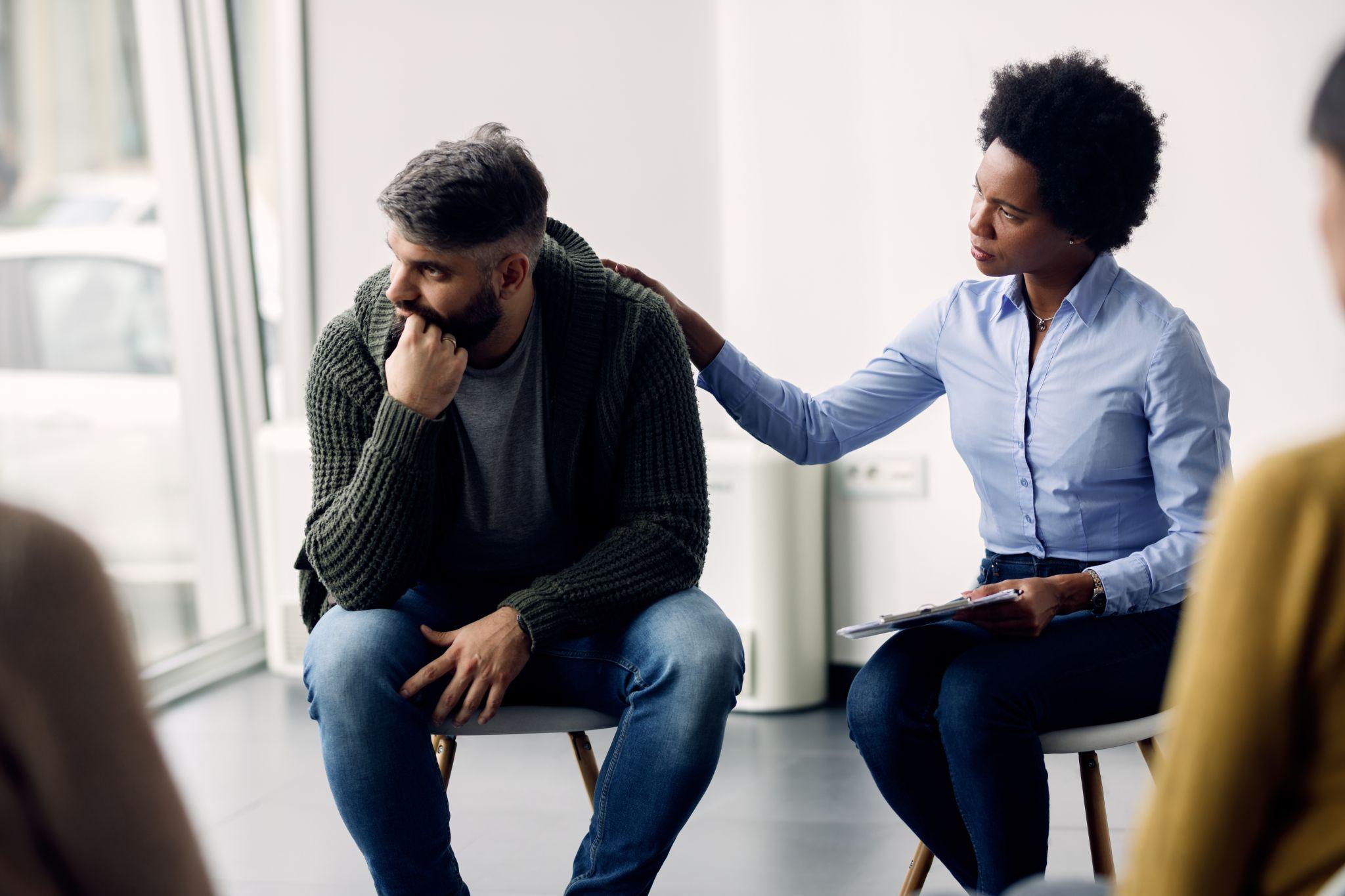 Female therapist supporting a man who is talking abut his issues during group meeting.