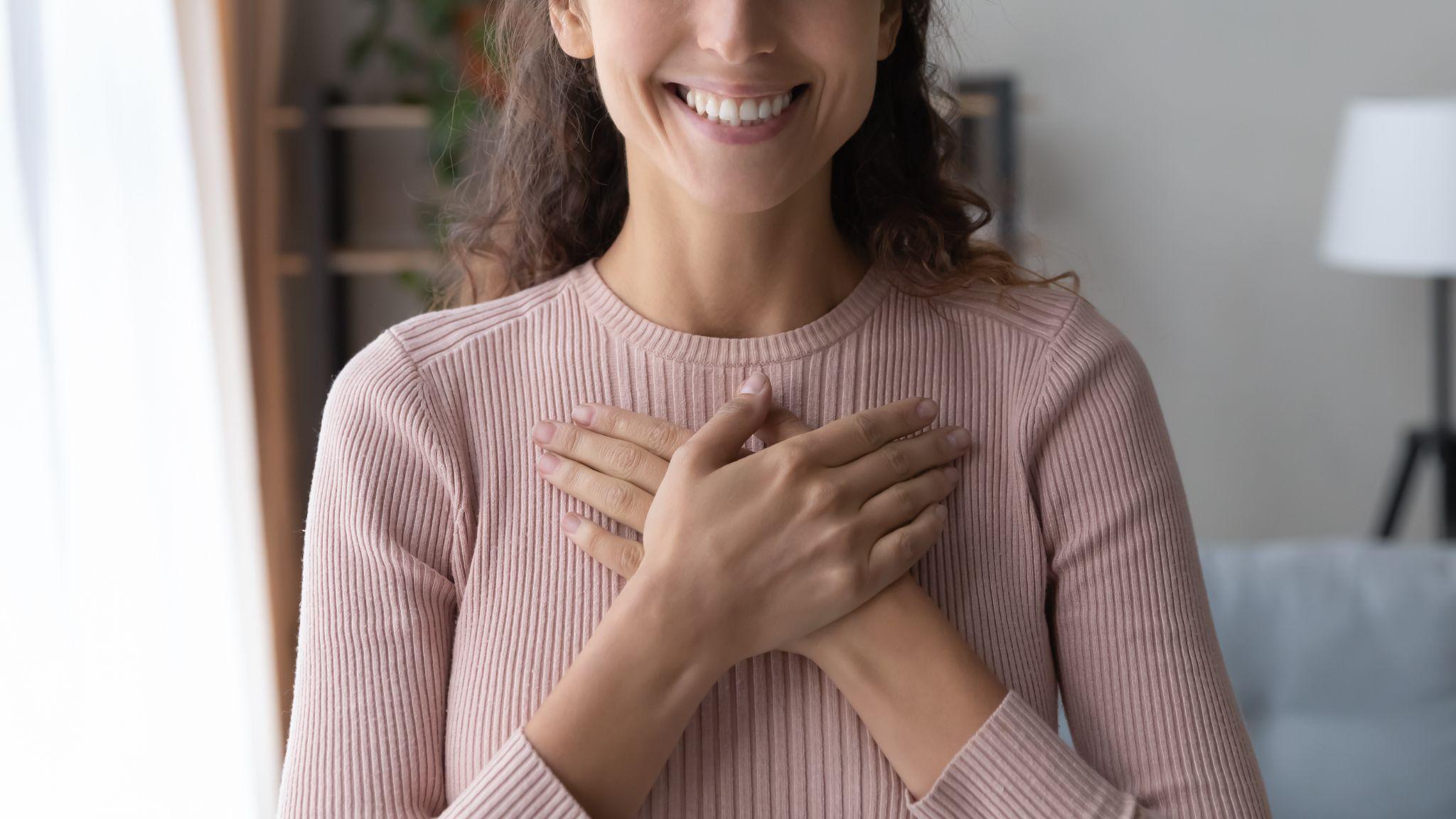 Happy sincere female holding folded hands on chest.