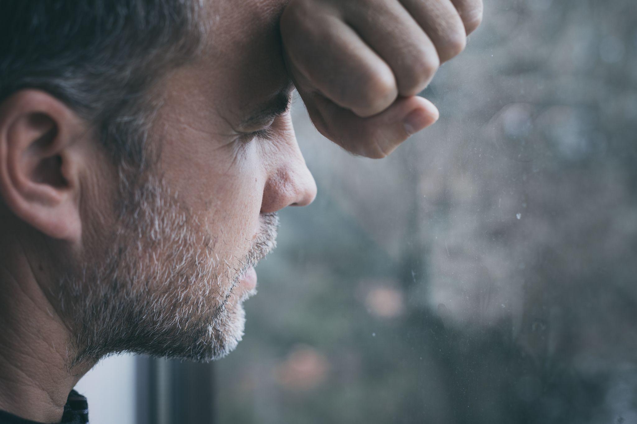 sad man standing near a window