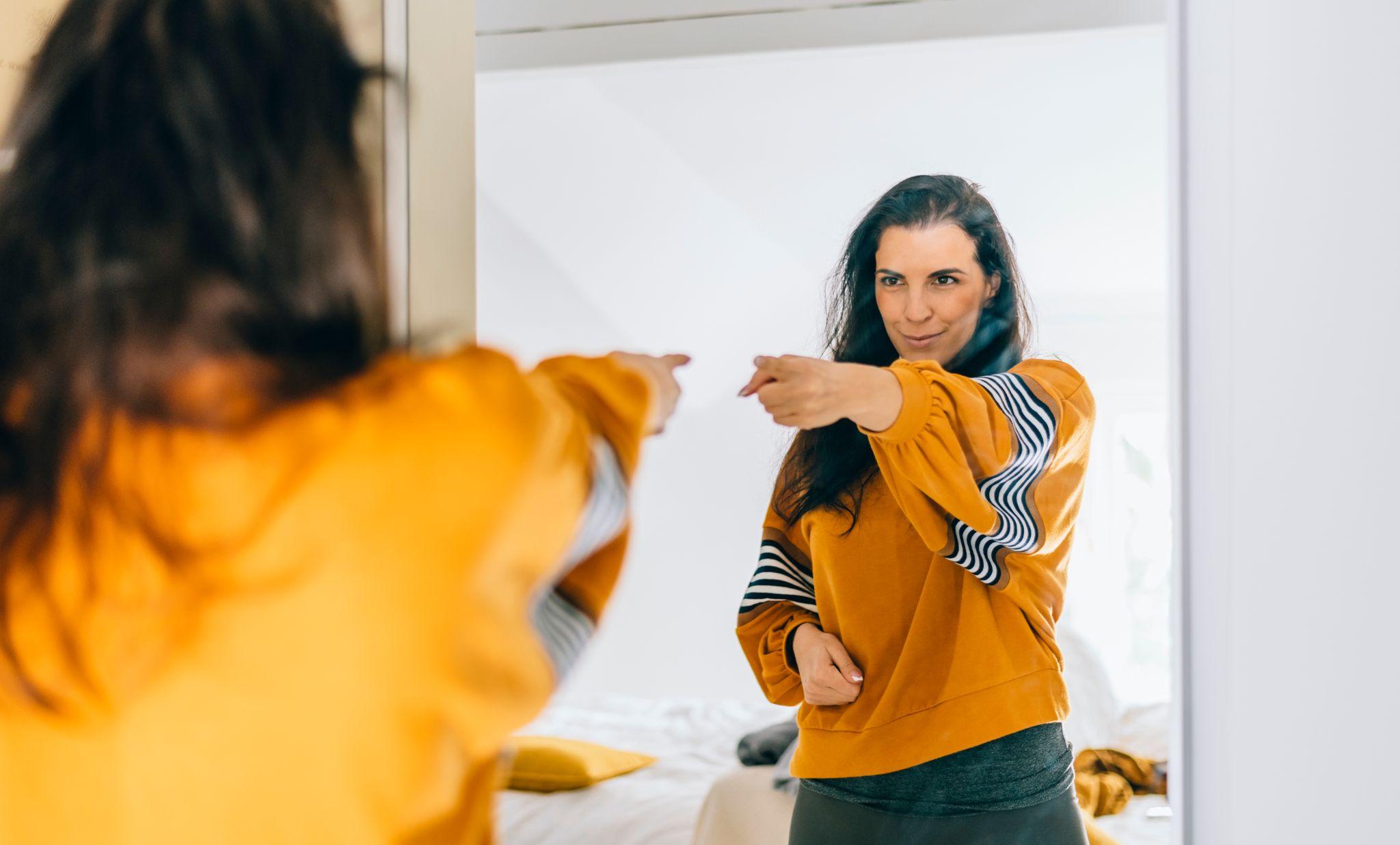 Self confident single woman pointing finger at reflection in mirror dancing and felling good.