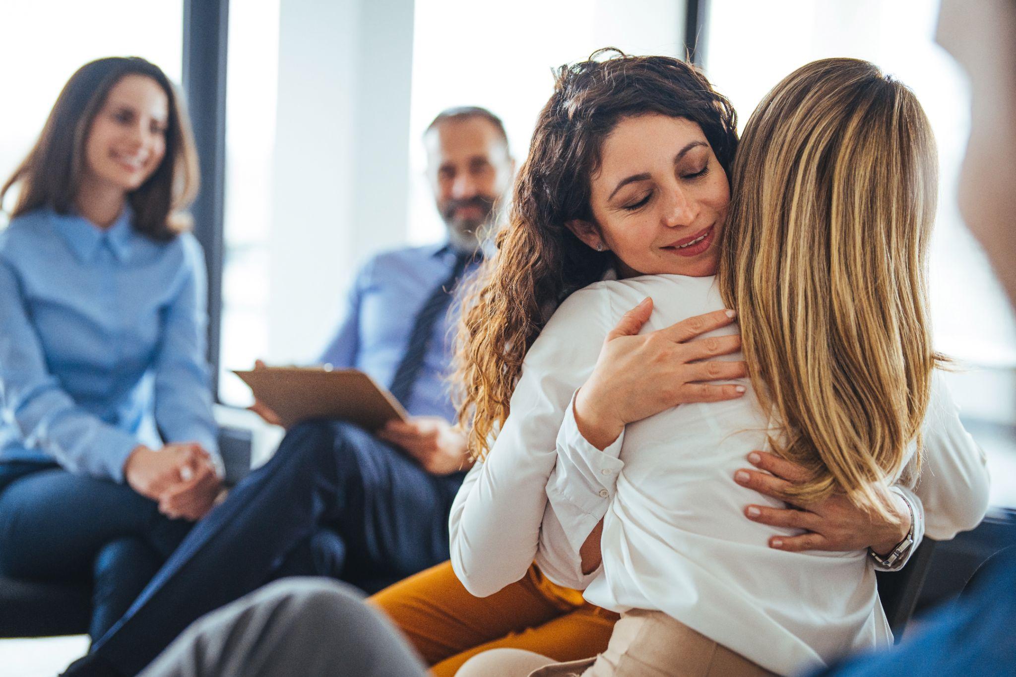 Young adult woman embracing and supporting friend during support group therapy session