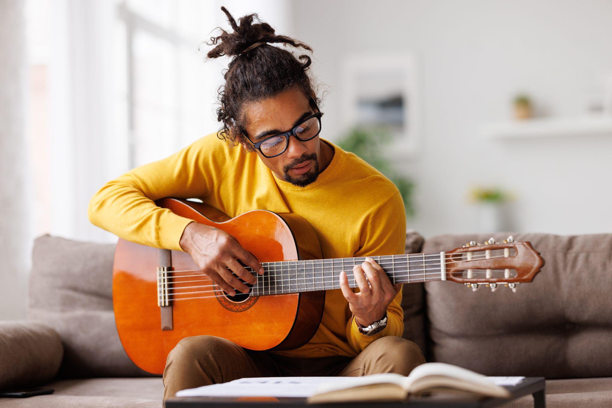 Young joyful african american man playing acoustic guitar at home