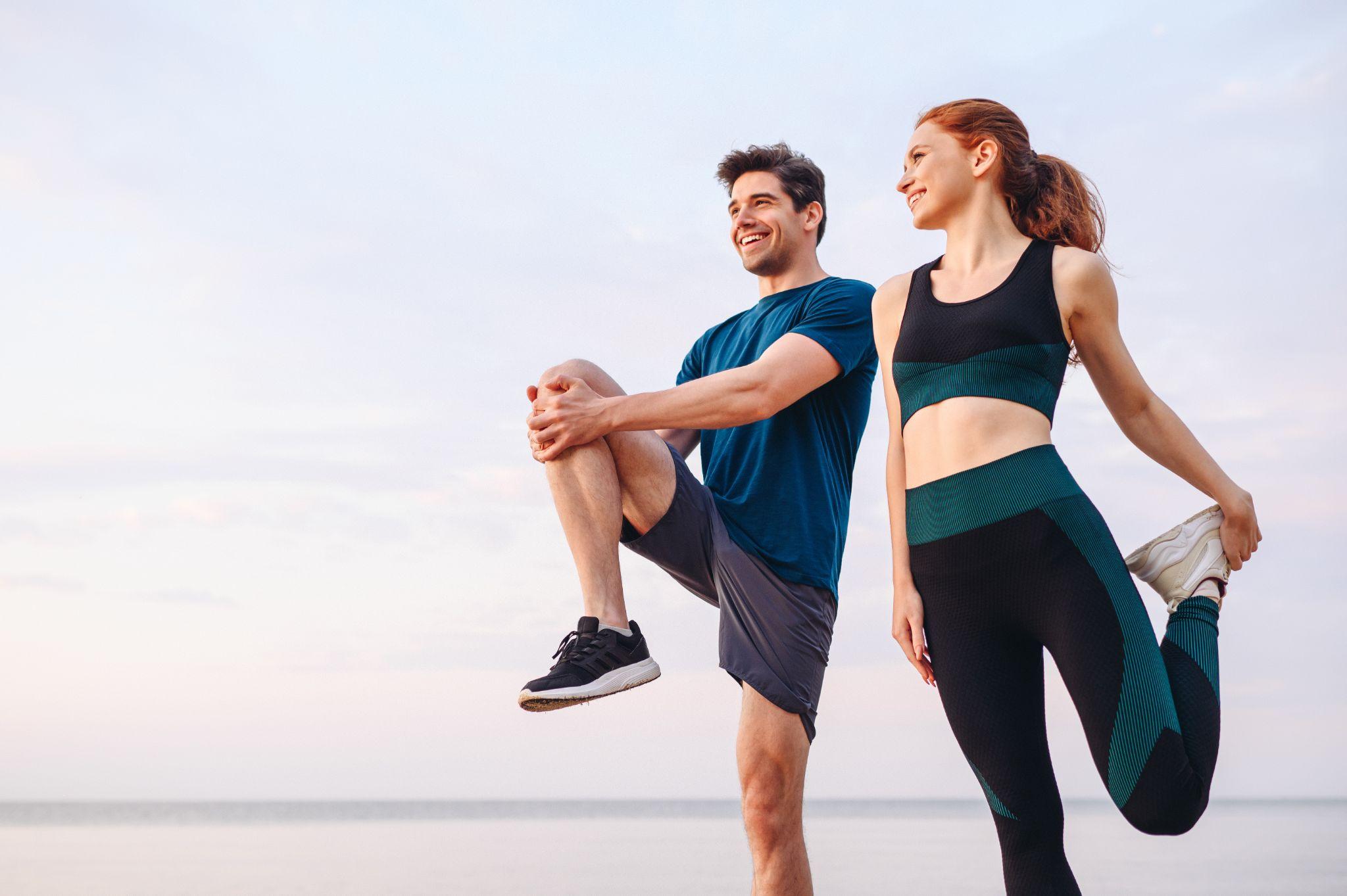 young two friend strong sporty sportswoman sportsman in sport clothes warm up training do stretch exercise on sand sea ocean beach outdoor jog on seaside in summer day morning.