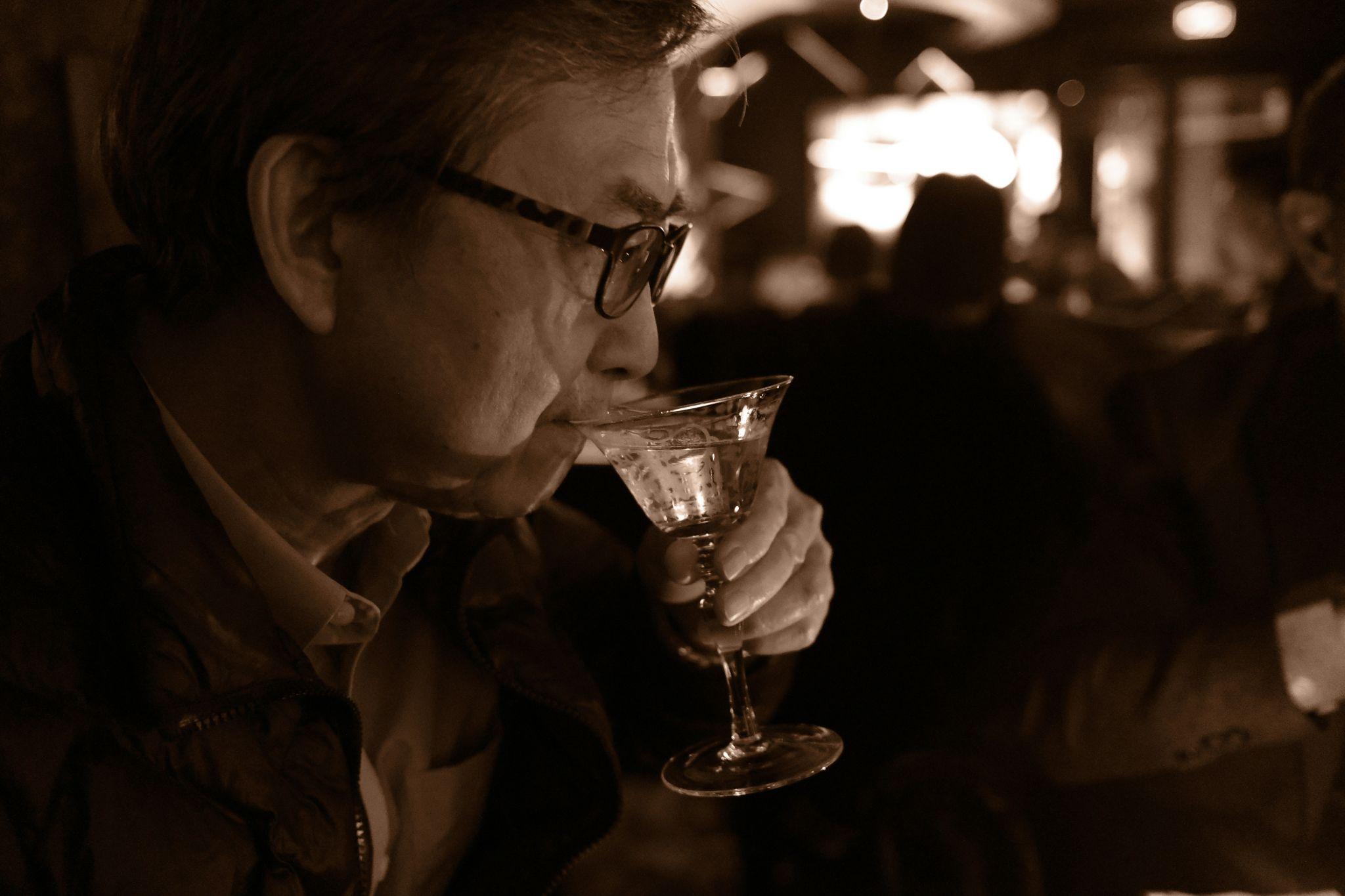 A elderly man drinking from a wine glass in a bar