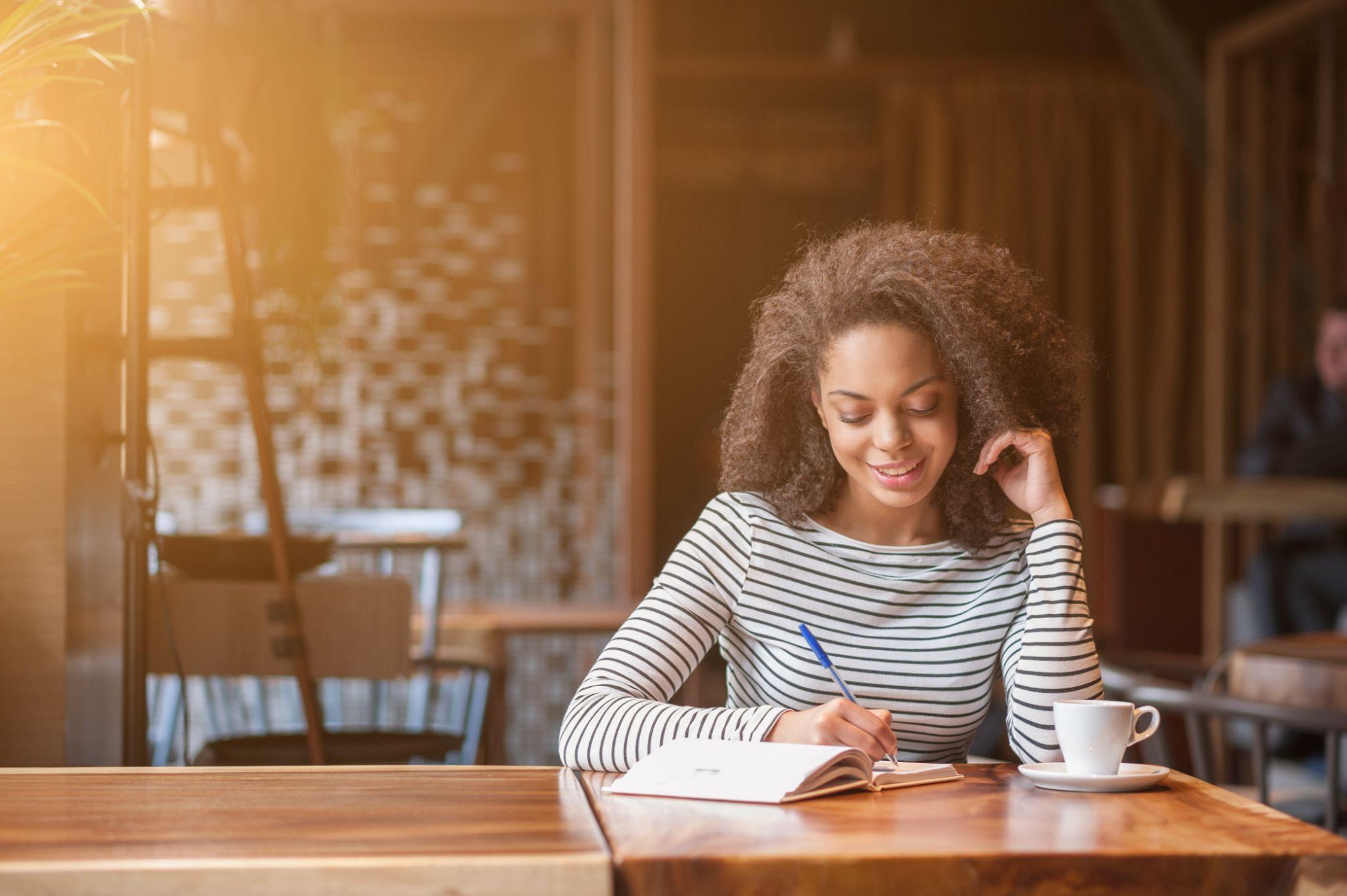 Cheerful young woman is writing in notebook