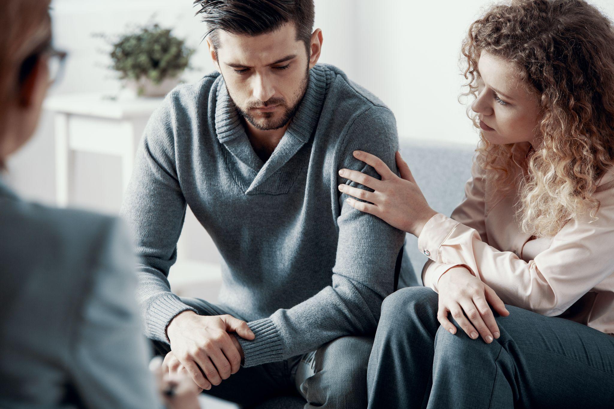 Female counselor writing in clipboard and talking to male patient in office