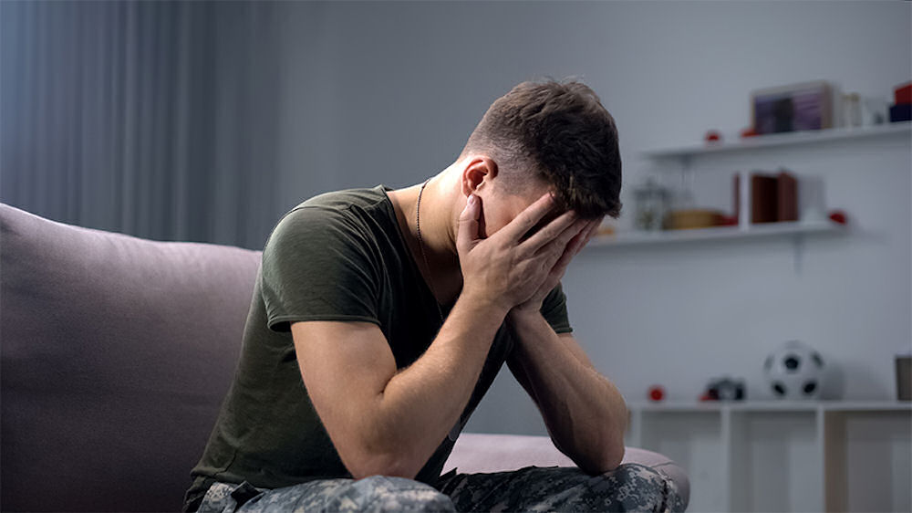 Man in military fatigues holding his face in shame during therapy
