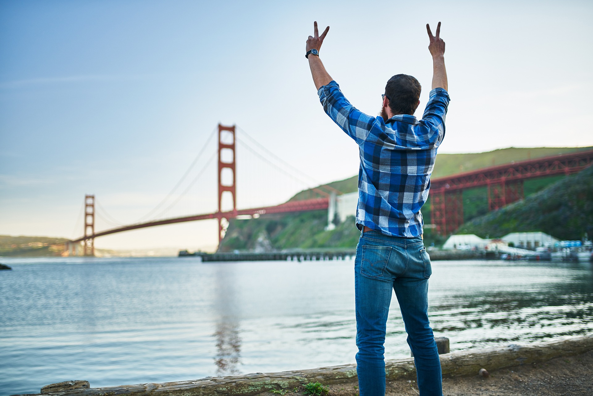 Man holds up two peace signs while looking out at San Francisco Bay and Golden Gate Bridge
